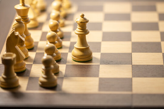 A set of wooden chess pieces arranged on a chessboard, ready for a game. The background is a blurred room, highlighting strategy and competition