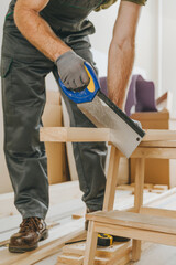 Close up of carpenter cutting a wooden board with a saw in his workshop