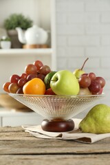 Glass vase with different fresh fruits on wooden table
