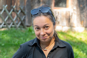 A woman smiling against a background of a wooden fence and trees.