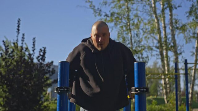 Man doing triceps dip exercise on parallel bars with extra weights at open gym.