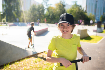 portrait of a boy in a cap with a scooter, in front of a skate park with children skating there