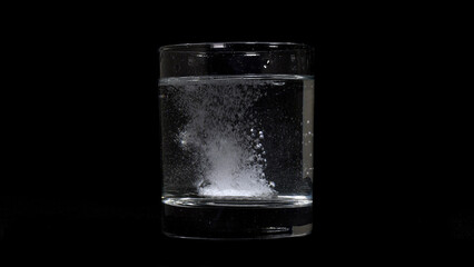 Image of medicine melting in glass on black background.