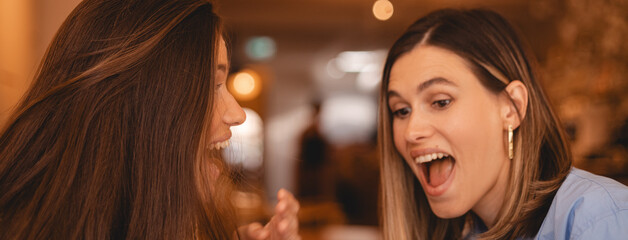 Overjoyed happy excited two women say wow, glad to receive text message informing salary, rejoices good news, stares at mobile phone, gestures actively from happiness, video call. Girls rest in cafe