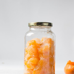 tangerine cheong in a glass jar on a white background, korean tangerine cheong in a transparent jar, tangerine in sugar syrup, process of making tangerine cheong