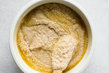 Overhead of moi moi mixture in a white ceramic bowl, top view of nigerian bean pudding being mixed, process of making nigerian moi moi