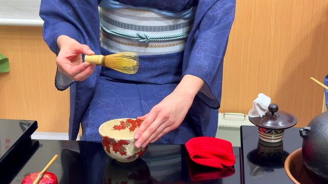 Preparation of Matcha involves woman whisking ground green tea powder into frothy, bright drink. Rooted in Japanese tradition, tea-making ritual focuses on mindfulness and connection to nature.