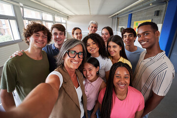 Cheerful selfie of young group of students taking a photo looking at camera with big smiles with their female teacher in the classroom, celebrating the back to school.