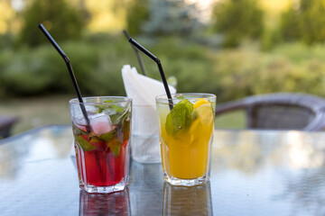 Two glasses of drinks with straws in them sit on a table