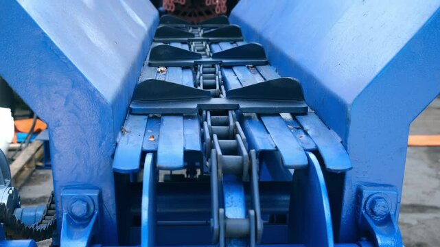 Blue industrial conveyor belt for moving logs from wood debarking machine. Modern equipment for timber production, tree trunk processing manufacturing at sawmill, lumber mill, wooden factory plant.