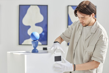 Minimal side view portrait of young Asian man working as art curator and setting up modern art...