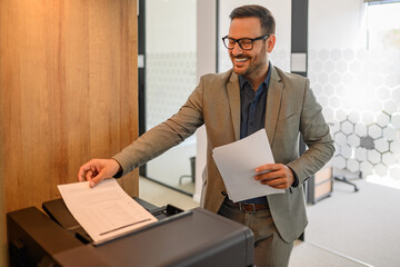 Portrait of smiling male printer smiling and putting sheet of paper into photocopier machine in office