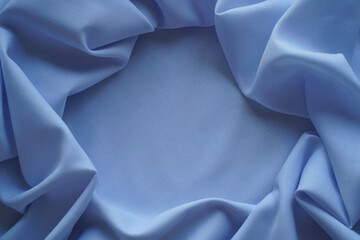 Blue textile background. Template with a frame of folds of plain cotton fabric. Close-up of threads of woven material, top view, copy space in the center.