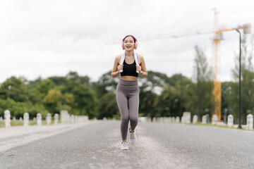 Road to Wellness: Joyful young Asian woman finds her stride, energized and smiling while running outdoors, embracing a healthy lifestyle. 