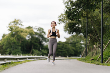 Invigorated Morning Run: Young Asian woman enjoys her outdoor workout, headphones in, embracing the tranquility of nature's gym. 