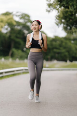 Active Lifestyle: Young woman jogging outdoors with headphones, a towel slung over her shoulder, embracing a healthy and energetic lifestyle.  