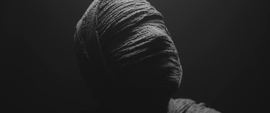 A mummy of a woman against the dark background raises her head and looks around 