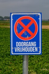 A blue European traffic sign: No stopping or parking.
Text in Dutch: Keep Passage Free.