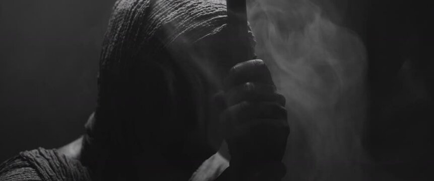 A mummy of a woman holds a walking stick on the dark background