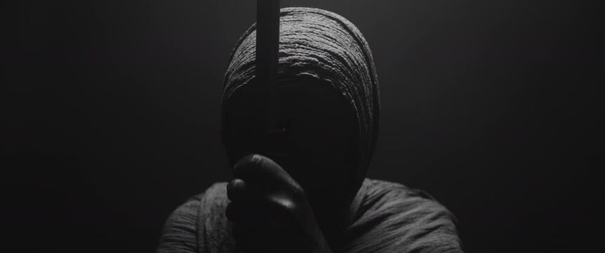 A mummified woman with a long stick against the dark background 