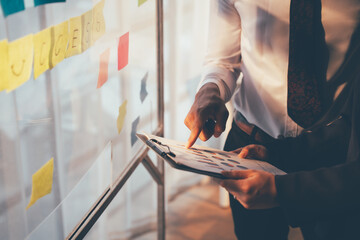 business man sticking adhesive notes on glass wall in office and discussting with team.