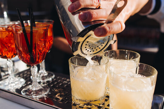 Bartender working, beautiful row line of different coloured liquor alcohol cocktails on a open air party in a bar, and others on catering banquet on event, barman mixing drinks and beverages in club