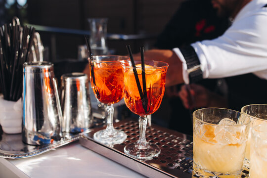 Bartender working, beautiful row line of different coloured liquor alcohol cocktails on a open air party in a bar, and others on catering banquet on event, barman mixing drinks and beverages in club