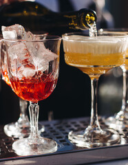 Bartender working, beautiful row line of different coloured liquor alcohol cocktails on a open air party in a bar, and others on catering banquet on event, barman mixing drinks and beverages in club
