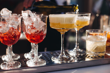 Bartender working, beautiful row line of different coloured liquor alcohol cocktails on a open air party in a bar, and others on catering banquet on event, barman mixing drinks and beverages in club