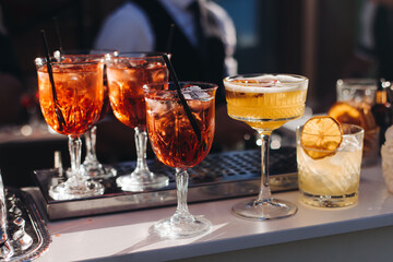 Bartender working, beautiful row line of different coloured liquor alcohol cocktails on a open air party in a bar, and others on catering banquet on event, barman mixing drinks and beverages in club