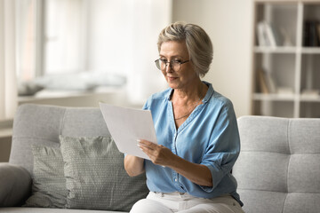 Older woman read paper letter with focused expression, read formal correspondence, review financial...