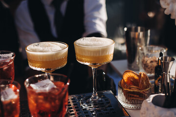 Bartender working, beautiful row line of different coloured liquor alcohol cocktails on a open air party in a bar, and others on catering banquet on event, barman mixing drinks and beverages in club