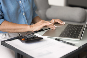 Woman using laptop sit at desk, calculator and document nearby, close up view, engaged in financial management, paying bills, control household expenses. Digital literacy, independence, online banking