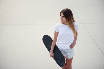 Young attractive girl in a white t-shirt and denim shorts holding skateboard. © gorynvd