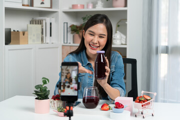 Smiling young beautiful Asian reviewing tasty mixed strawberry and cherry juice detox drinks,...