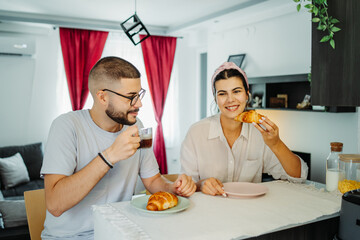 Two friends male and female are eating croissant for breakfast