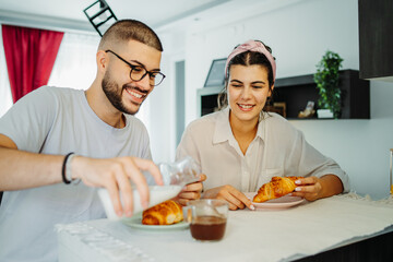 Two friends male and female are eating croissant for breakfast
