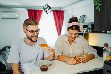 Two friends male and female are eating croissant for breakfast