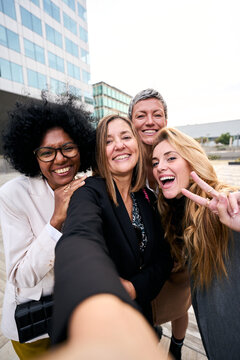 Vertical. Group smiling multiracial empowered business women taking selfie fun in formal suit looking at camera gathered outside work building. Positive emotion team office together in break outdoor