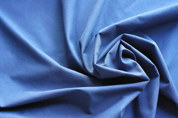 Abstract background with blue fabric twisted in a spiral. Cotton textile, folds, rays diverge to the edges. Top view, close-up, copy space.