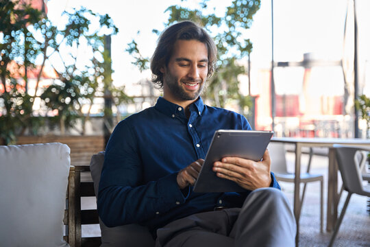 Happy young European business man executive holding pad computer at work. Male professional employee using digital tablet fintech device sitting outside office checking financial online market data.