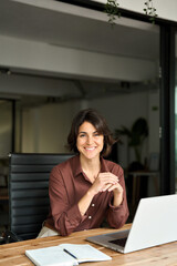 Vertical portrait of confident businesswoman leader in her 30s at work desk. Smiling Hispanic young...