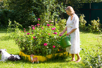 a woman in a white dress with a watering can in her hands is watering flowers in the garden....