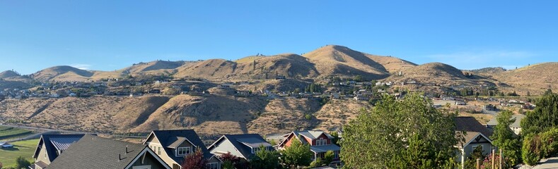 A panoramic view of the arid hillsides above the rooftops of houses at Chelan, Washington on a beautiful summer day_06212024_0001.