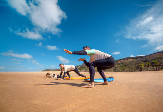 Family of surfers learning to surf in the Atlantic ocean. First surfing lesson. Amateur surfer. Surfing training. Photo for surfing school advertising on social media. - Powered by Adobe