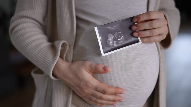 A glowing pregnant woman cradles her bump while joyfully holding an ultrasound photo, symbolizing hope