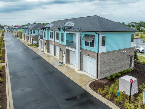 American real estate development in South Carolina, view of duplex town house with turquoise vinyl siding, double garage with white garage door, dark window frames and gutters 