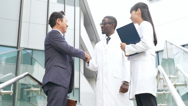 ロビーで握手するビジネスマンと白衣の多国籍技術者グループ
