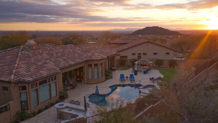 An aerial view of a desert landscaped backyard featuring a travertine pool deck with an outdoor kitchen, fireplace, pool and spa.