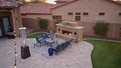 An aerial view of a desert landscaped backyard featuring a travertine pool deck with an outdoor kitchen, fireplace, pool and spa.
